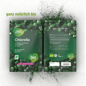 Abgebildet sind zwei grüne Packungen gse.organic.supplements Naturland Bio Chlorella (Tabletten), umgeben von grünen Tabletten. Die Verpackung zeigt deutschen Text, Umweltetiketten sowie Symbole für vegan und Vitamin-B12-Quelle.